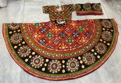 Black and red garba chaniya choli laid flat — red diamond lattice yoke and circular mirror medallions on black with a mirrored choli