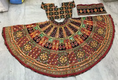Maroon dandiya lehenga laid flat — dense gold and green embroidery with mirrors, black teardrop yoke and a matching embroidered choli