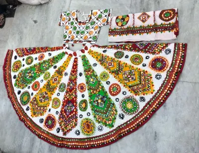 White dandiya chaniya choli laid flat — Kutchi mirror medallions on an off-white ground with a scalloped maroon border