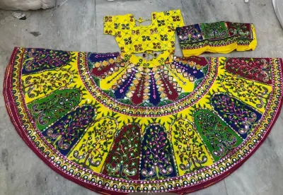 Yellow garba chaniya choli laid flat — peacock and tree-of-life panels in green and purple with mirrored teardrops at the waist