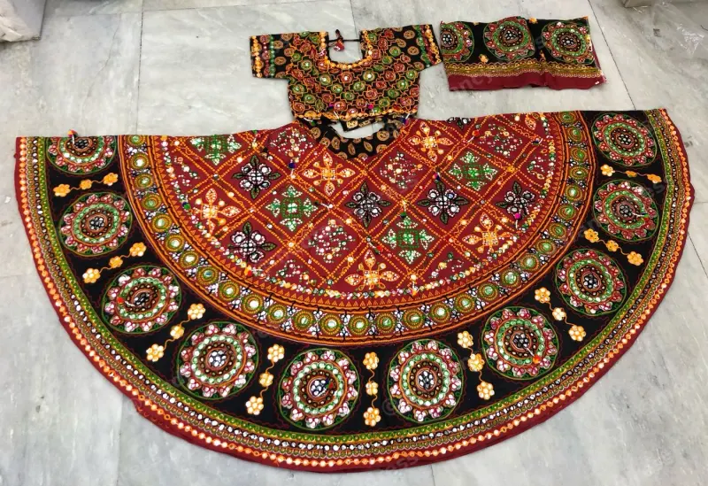 Black and red garba chaniya choli laid flat — red diamond lattice yoke and circular mirror medallions on black with a mirrored choli