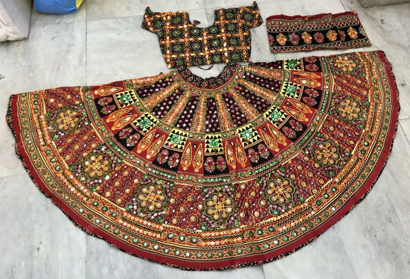 Maroon dandiya lehenga laid flat — dense gold and green embroidery with mirrors, black teardrop yoke and a matching embroidered choli